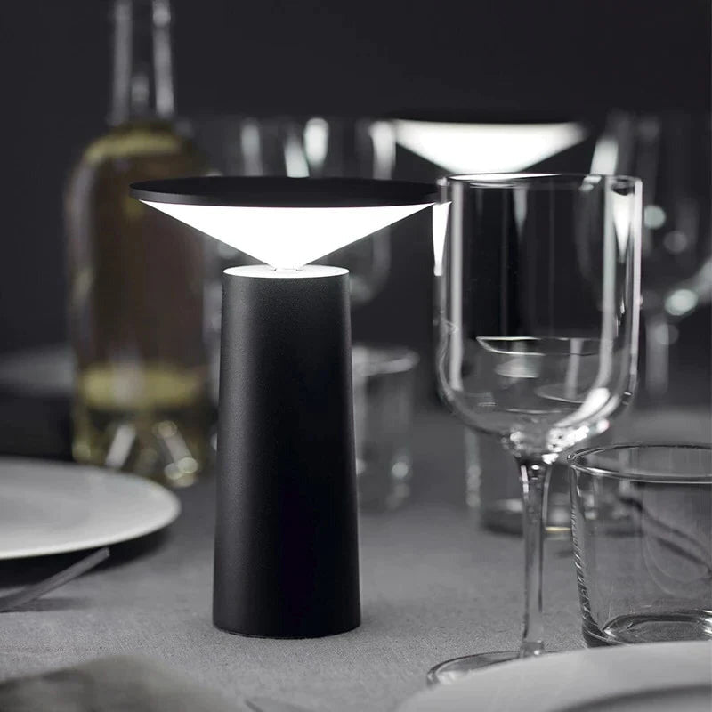 Black table lamp on a dining table with wine glasses and plates in the background